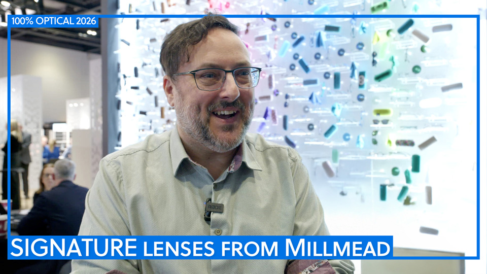 A laughing man stands in front of a light wall with a rainbow of spectacle frames, lenses and cases displayed