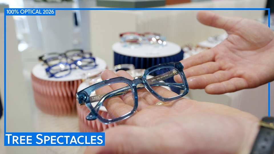 Hands hold a glossy crystal blue pair of spectacles. In the background are circular props to display more spectacles