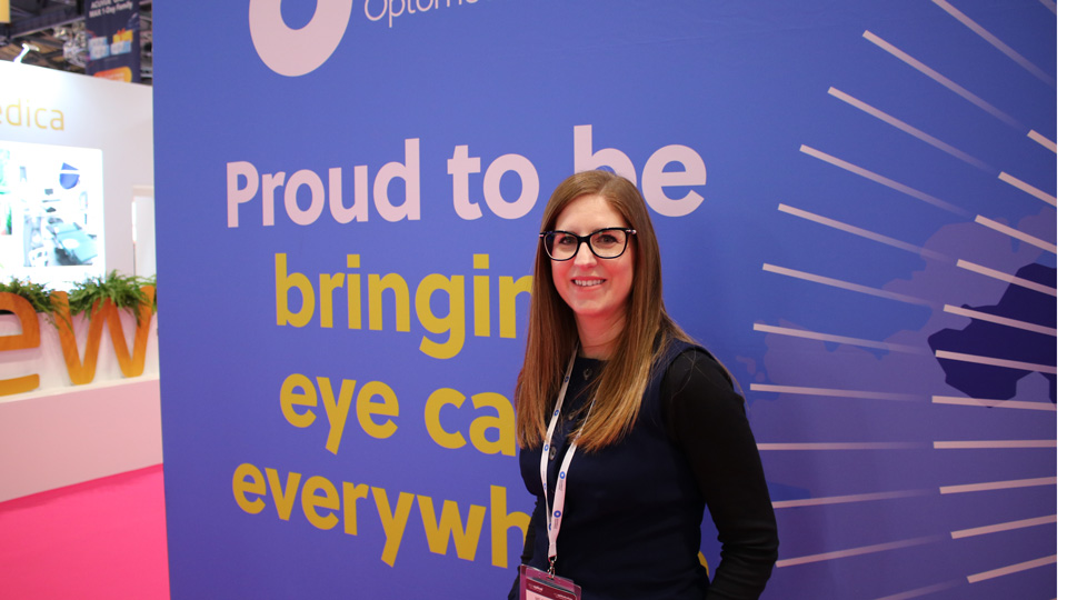 Serena Box stands in front of a blue wall on the AOP stand at 100% Optical 