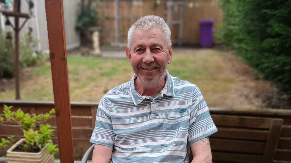 Robert sits at a table in the garden smiling