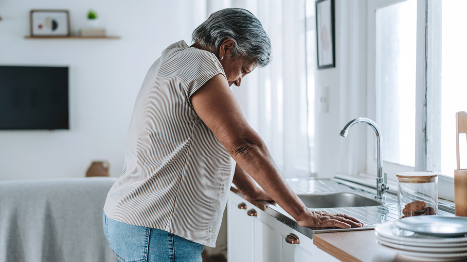 A middle aged woman leans against a kitchen sink