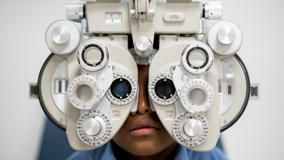A body sits behind a phoropter head during an eye examination