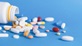 A white bottle on its side with a range of colourful medicine pills and capsules spilling out of the bottle.  