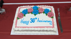A white cake with blue and pink roses made of icing and blue script: Happy 30 anniversary