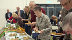 Patients, members of the community, and friends gather around a table of food and drinks for the celebration