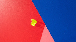 A close-up of a red, pink and blue geometric artwork with a yellow blob of paint