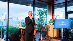 James holds a microphone and presents a speech at the business anniversary event