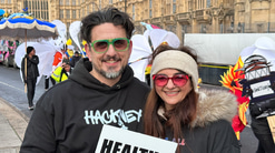 Two people pose in the New Years Day Parade in London holding a healthy eyes sign and wearing Hackney jumpers
