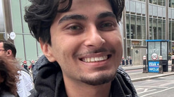 Danyal Nasim is standing on a busy city street wearing a jacket and backpack