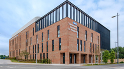A large brick building, with a steel pillar construction, large windows, and shrubbery around