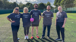 A group of five people, two women and three men, in grey Freedom Vision branded t-shirts. One holds a pink and blue football