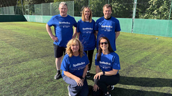 A group of five people, three stood behind and two knelt in front. There are three women and two men all in blue SpaMedica-branded t-shirts