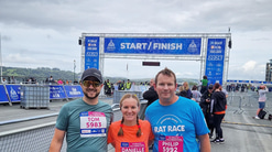 Three members of a practice team stand together at the finish line of the Plymouth half marathon