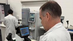 David in a white lab coat using a machine on a lens