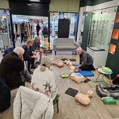 Members of the public sit in a semi-circle of chairs watching a CPR demonstration  