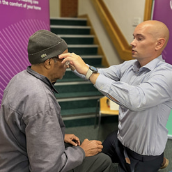 Matt is kneeling with a patient to adjust glasses on them