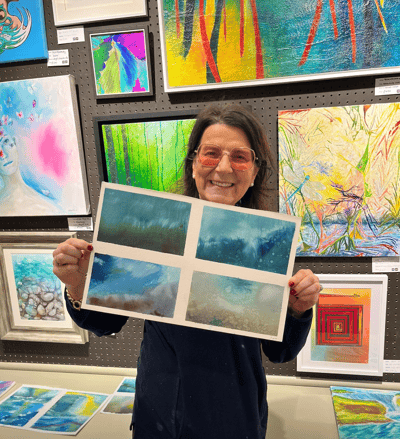 Francesca Marchetti stands with a painting she has created against a backdrop of other paintings