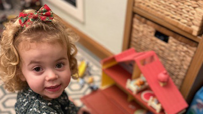 Jessy is photographed playing with a doll’s house. One of her pupils is larger and darker than the other