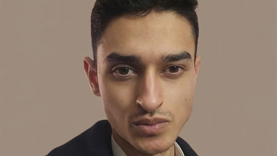 Bilaal wears a black suit jacket over a white shirt and red tie