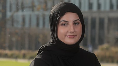 Juwaria is photographed outside with a green field behind her. She wears a black top and headscarf