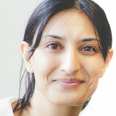 Dr Manbir Nagra smiles at the camera. She has dark hair which is pulled back, a white peter-pan collar blouse and a red cardigan