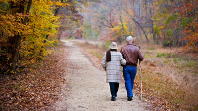 Two older people walking down a country path in autumn