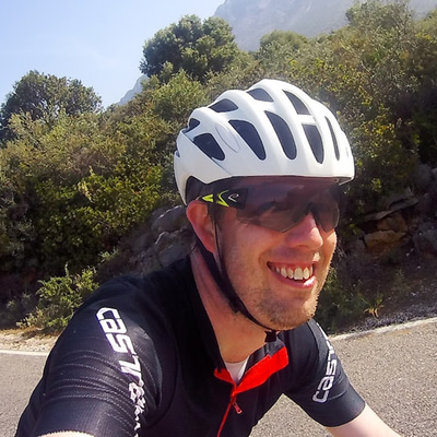 Man smiling wearing a bicycle helmet and sunglasses on his bike on a country road