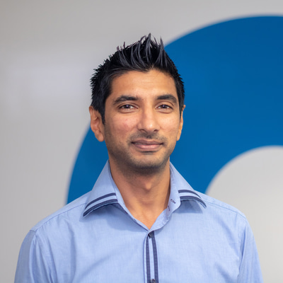 Vijay Anand smiling looking into the camera. He has black hair and is wearing a pale blue shirt