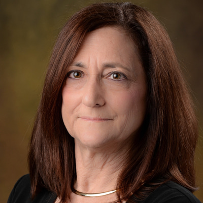 In a formal headshot image, Dr Sandra Block sits at an angle to the camera and smiles 