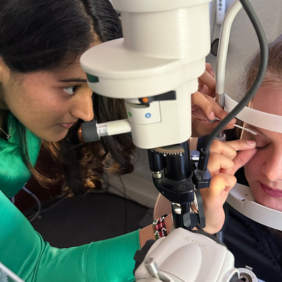 The image is taken from above and through an optical instrument as Palak gently touches a cotton bud to the eyelid of a patient 