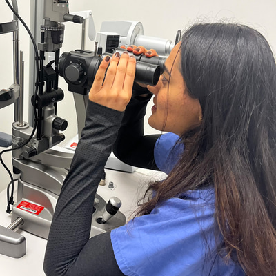 A side-on picture of Palak in blue scrubs, looking into the viewfinder of an instrument in clinic