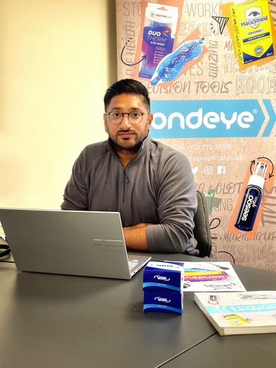 Vijay Chauhan sits at a desk with a laptop and a package with the Volk logo. In the background is an artistic wall with the Bondeye Optical branding