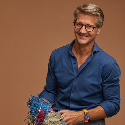 Francois van den Abeele in a photoshoot, we wears a shirt and jeans and holds a mass of fishing nets 