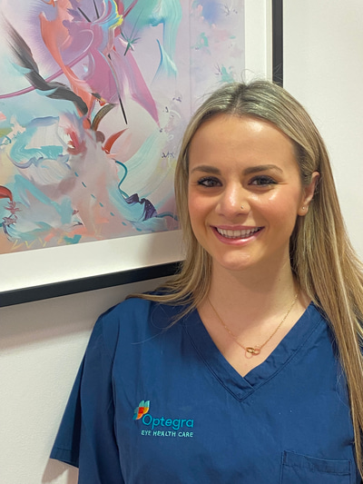 A young woman with straight blonde hair and blue doctor’s scrubs smiles at the camera