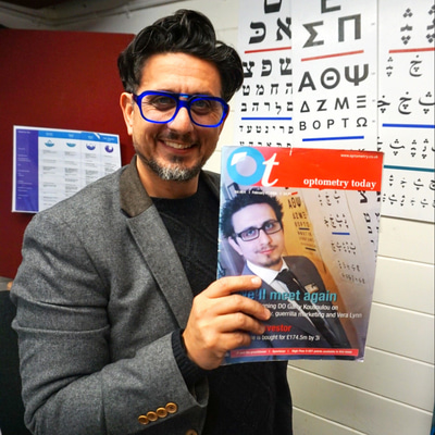 Garry stands in his practice by a wall of Snellen charts in multiple languages, he holds up a copy of a 2008 front cover of Optometry Today featuring himself standing in the same position.
