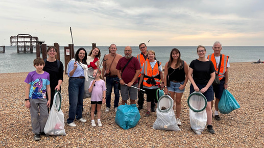 A group of people gather on a beach holding litter picking equipment for a beach clean