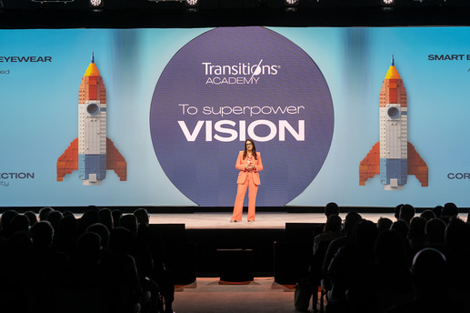 Chrystel, wearing a salmon pink suit, stands before screens with a lego rocketship stating ‘Superpower vision’
