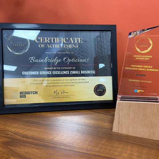 A framed certificate for Bainbridge Opticians’ customer service excellence alongside a glass and wood trophy