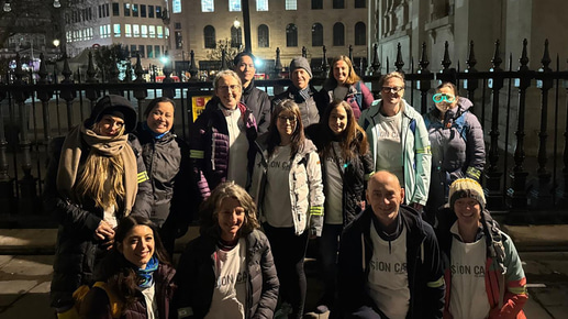 A group of 14 people gather in rows on a London street at night. They are wrapped up for a nighttime walk in the cold with t-shirts displaying the Vision Care logo