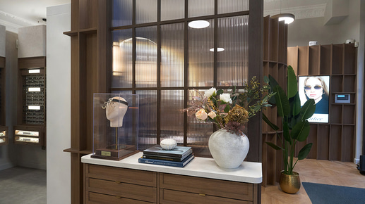A practice with dark wood panelling and light fluted glass windows. Display cases have large marble vases, coffee table books dedicated to eyewear design, and a case with an old style of trial lens frame