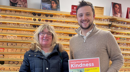 Tom stands beside a representative from a charity, he holds a sign advertising the practice’s fundraising challenge