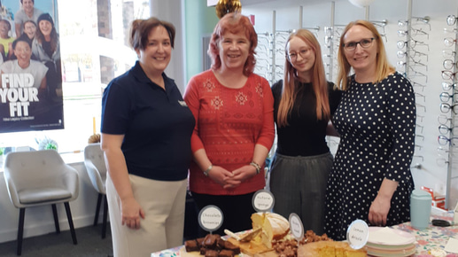Four women gather around a table full of cakes in an optical practice