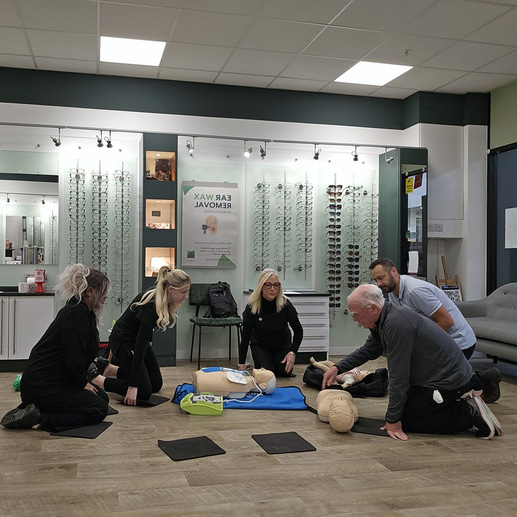 A group are knelt around an instructor and a CPR training model 