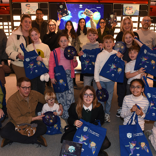 A group photo of the children and adults who attended the Class of Myopia event, each holding a blue tote bag with space characters