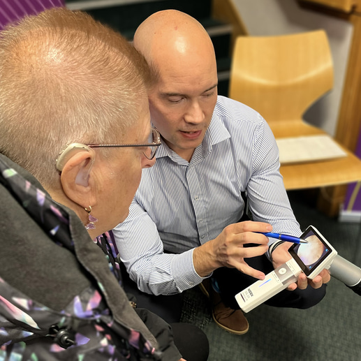 Matt is crouched before a patient, pointing to a handheld imaging device, describing what the image is displaying