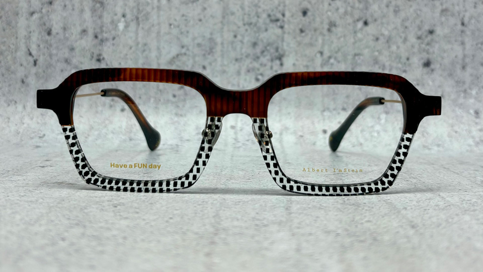 A pair of Albert I’mStein spectacles. The frames are squared, the top half is a fluted texture in deep red-brown, the bottom half is clear with black squared dot pattern