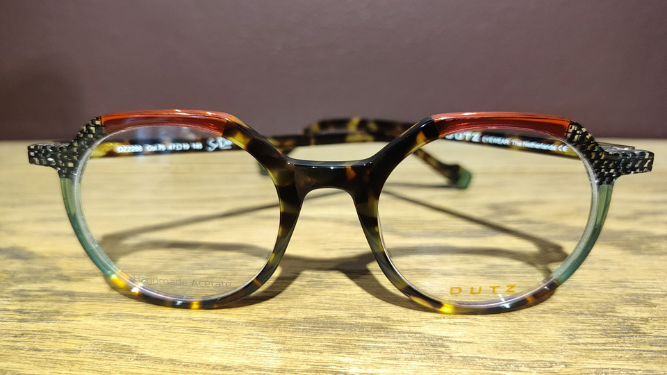 A hexagonal shaped frame in a patchwork of colours and patterns including tortoiseshell, red, checkered clear acetate, and green