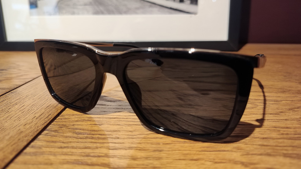 A pair of dark sunglasses in black with a low metal browline, the effect is very flat and angular – almost like a shield style