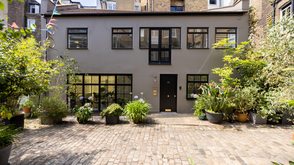 The outside of the practice is a grey building with large windows, an abundance of potted plants and shrubs, and bunting strung between buildings. The effect is bright, lively, and modern