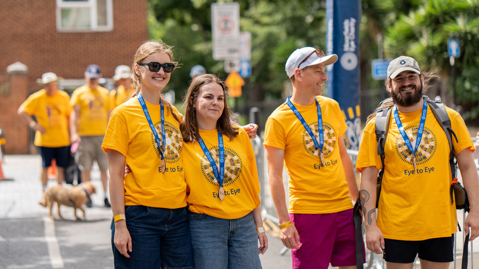 Four participants in yellow t-shirts stand in a line. All are wearing blue participation medals around their necks
